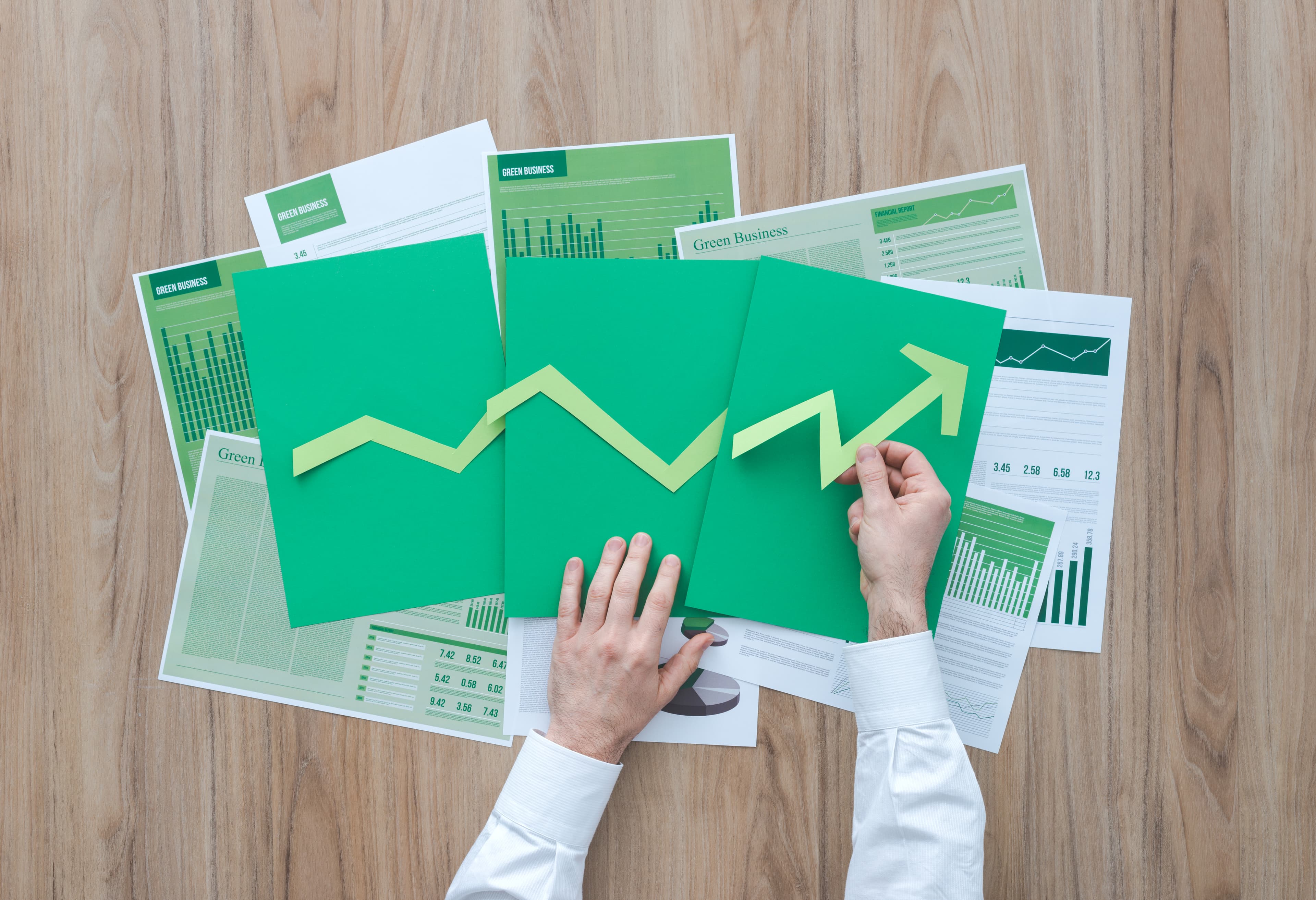 Businessman composing a successful financial chart with green arrow pointing up, he is using paper cuts, financial achievement and green business concept